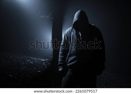 Hooded man in the dark forest at backlight