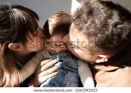 mother and father giving a kiss to their baby, natural light indoors, royal family photo