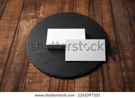 Blank white business cards and round slate plate on wooden background. Template for ID.