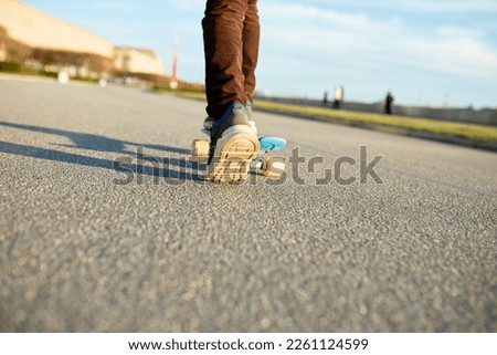 Closeup low view picture of feet of kid skateboarding on city streets in warm spring day, kicking asphalt with leg to accelerate, enjoying weekend and urban sports. Leisure activity