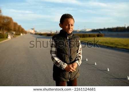 Upset worried black boy kid standing on background with city park holding his stomach with painful facial expression and miserable look, feeling pain in belly after training outdoor Royalty-Free Stock Photo #2261124681