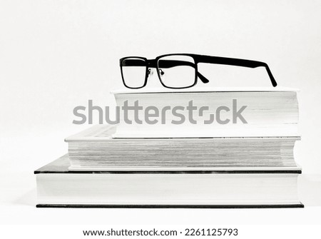  Three thick books and glasses as a visual aid as black and white picture                              