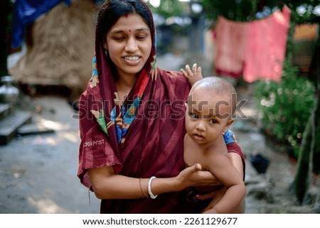 South asian young mother holding her baby son in a village environment, straw hatch in background, woman wearing shari  Royalty-Free Stock Photo #2261129677