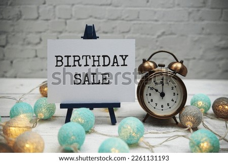 Birthday Sale text and alarm clock on white brick wall and wooden background