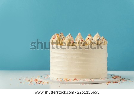 Birthday cake with white cream cheese frosting decorated with multicolored lit candles on a blue background. Happy Birthday concept. 
Tradition of making a wish while blowing out candles on a cake