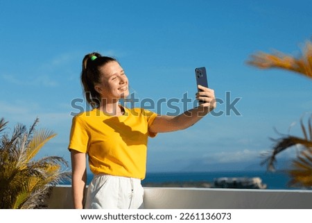 young beautiful happy woman blogger is taking selfie, picture of herself on frontal camera to social media of smartphone, cell mobile phone, smiling waving her hand, having video call, conversation
