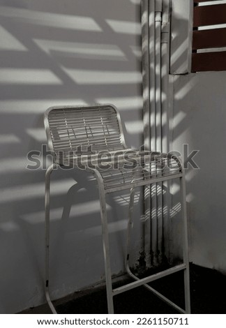 Beautiful sunlight shine through the white metal chair with white wall background. Space for text, Selective focus.