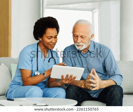 Doctor or nurse caregiver showing a tablet screen to  senior man and laughing at home or nursing home Royalty-Free Stock Photo #2261150765