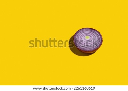 Single red onion cut in half on yellow background