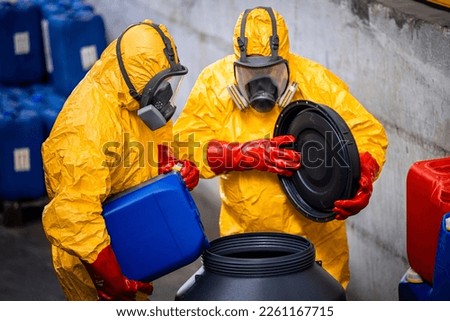 Workers in protective suit, gas mask, rubber gloves working in chemicals factory dealing with acid. Royalty-Free Stock Photo #2261167715