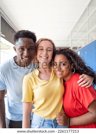 Three multi-ethnic young people laughing and looking at camera having fun on campus. High school, diversity  Royalty-Free Stock Photo #2261177213