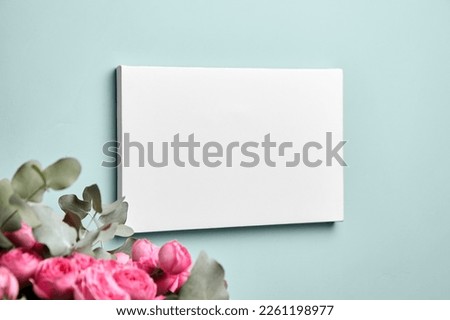 Blank picture canvas mockup hanging on green mint color wall and bouquet of pink roses with eucalyptus leaves. Empty blank photo frame, interior decor