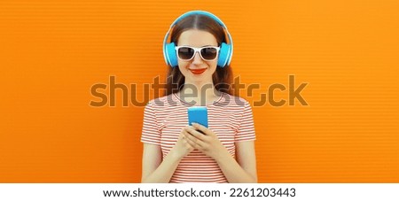 Portrait of smiling young woman in headphones listening to music with smartphone on orange background