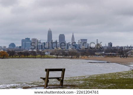 A empty bench sits along Lake Erie's shore on a wintery, stormy day with Cleveland', Ohio skyline in the background at Edgewater Park.