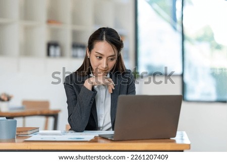 Young Asian businesswoman holding a pen sitting and analyzing the details of management information Finance is happy at the desk in the office. Royalty-Free Stock Photo #2261207409