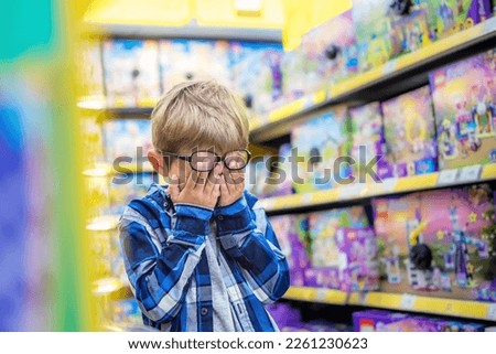 The little boy in the toy store is upset. The kid covered his eyes with his hands, crying. Child's tears in toy shop.  Royalty-Free Stock Photo #2261230623
