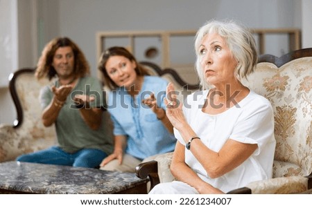 Dissatisfied mother-in-law siting on a chair against of a confused husband and wife on the sofa in the living room at home Royalty-Free Stock Photo #2261234007