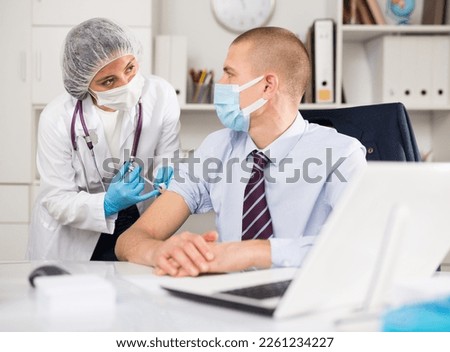 Medical nurse in safety gloves and protective mask making vaccine injection to a patient in health clinic Royalty-Free Stock Photo #2261234227