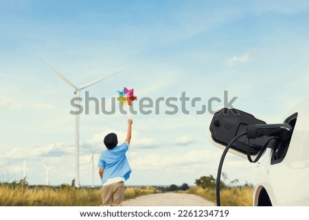 Progressive young asian boy playing with wind pinwheel toy in the wind turbine farm, green field over the hill. Green energy from renewable electric wind generator. Windmill in the countryside concept Royalty-Free Stock Photo #2261234719