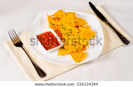 High angle view of a plate of golden spicy nachos or corn tortillas with tomato and chili salsa