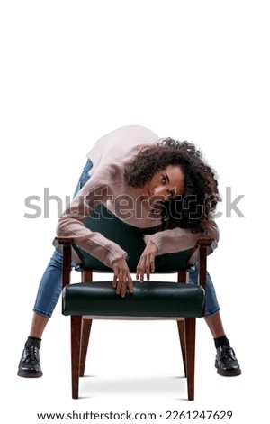 Young curly-haired woman hunched over a chair in front of her holding her long legs straight and looking bored, her arms dangling relaxed. She wears a pink sweater and jeans. Isolated on transparent o