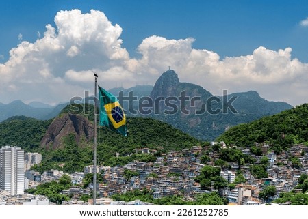 Brazilian flag in foreground and  Christ looking at Favela (Shanty Town) in Rio De Janeiro, Brazil Royalty-Free Stock Photo #2261252785