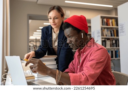 Motivated multiracial concentrated pensive students teammates at university library table discussing study project ideas. Help in preparing test exam from caucasian tutor to African American student. Royalty-Free Stock Photo #2261254695