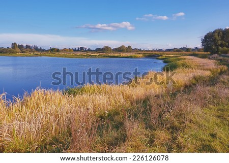 Autumn landscape - evening on river with trees on the banks and the clouds in the blue sky