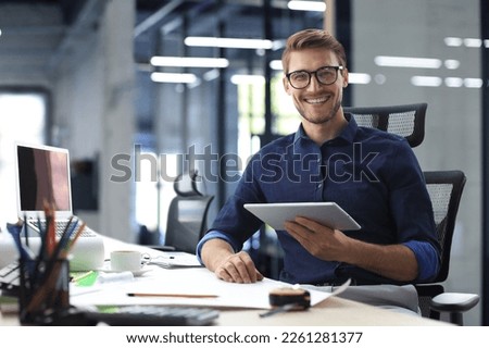 Young modern business man working using digital tablet while sitting in the office Royalty-Free Stock Photo #2261281377