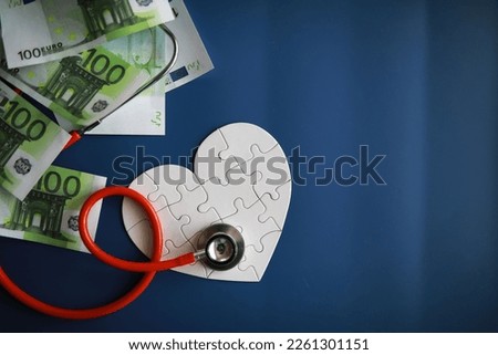 A stethoscope on money and a puzzle heart. Health insurance. Healthcare and medicine. How much is the treatment. Money and medicine. World Heart Day. World Health Day.