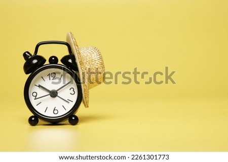 A picture of alarm clock with straw hat on copyspace yellow background. Flexible time working hours concept.