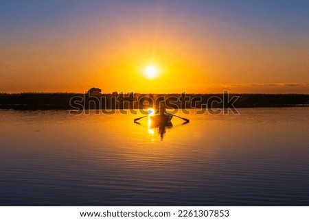 A classic rowboat against a backlit orange sunset in semi-darkness. Silhouette of a 60-year-old Caucasian male with oars in his hands in the rays of the sun Royalty-Free Stock Photo #2261307853