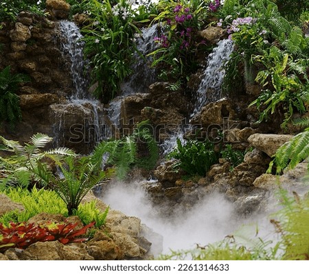 A waterfall surrounded by rocks and colourful plants with mist rising up from the pond area