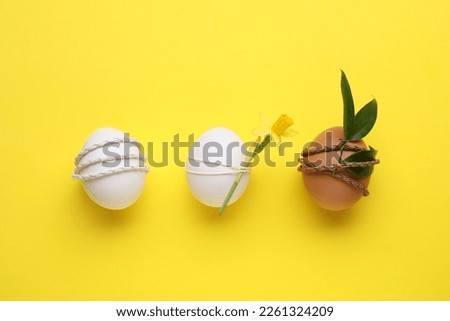 Easter eggs decorated with green leaves and flower on yellow background, flat lay