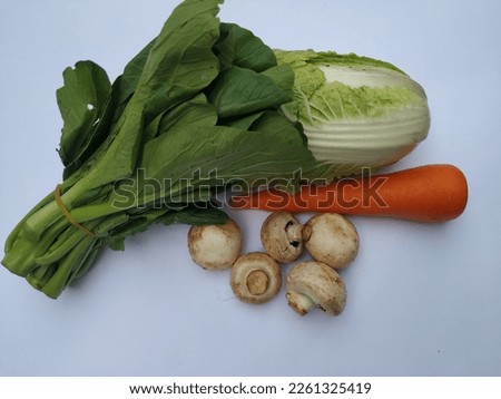 An isolated white  image of several vegetables which are a chinese cabbage, a carrot, mushrooms and a mustard green taken close up and  from top view angle