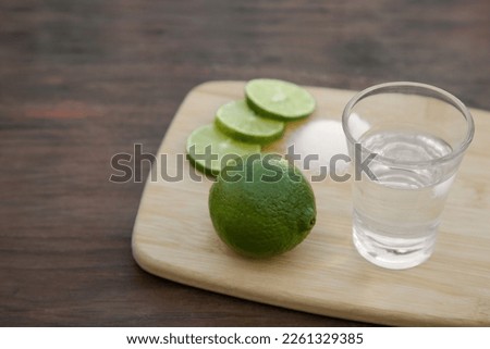 Mexican tequila shot with lime slices on wooden table, closeup and space for text. Drink made from agave