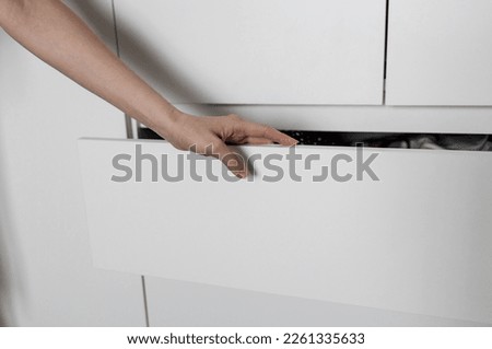 hand pulls out a shelf in a white cabinet. close up hand opening drawer Royalty-Free Stock Photo #2261335633