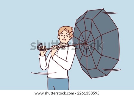 Man with umbrella turned backwards walks down street during severe life-threatening storm. Pedestrian in casual clothes caught in hurricane walking around city and needs shelter Royalty-Free Stock Photo #2261338595