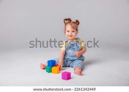 little baby girl is sitting on a white background and playing with colorful cubes. kid's play toy cubes
