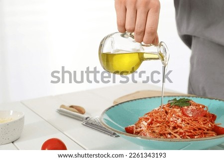 Food stylist pouring oil into spaghetti at white wooden table in photo studio, closeup