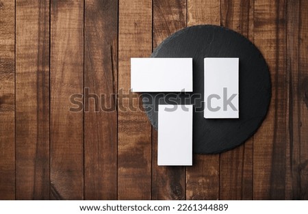 Photo of three blank business cards and round slate plate on wooden background. Branding ID template. Flat lay.