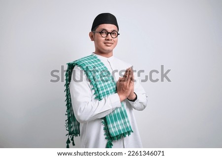 Asian Muslim man wearing white clothes smiling to give greeting during Ramadan and Eid Al Fitr celebration standing over white background Royalty-Free Stock Photo #2261346071