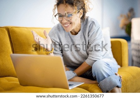 Modern happy young woman smile and have fun in video call computer online activity. Calling friends using internet and laptop connection. Smart female people sitting on yellow sofa with notebook pc Royalty-Free Stock Photo #2261350677