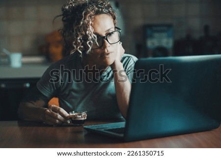 One adult woman using computer in early morning at home drinking an espresso coffee. Female people watching laptop with attention and concentration. Modern young lady work on notebook alone apartment