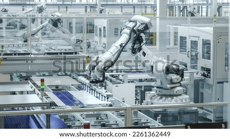 Automated Manufacturing Facility. White Industrial Robot Arm at Production Line at Modern Bright Factory. Solar Panels are being Assembled on Conveyor.