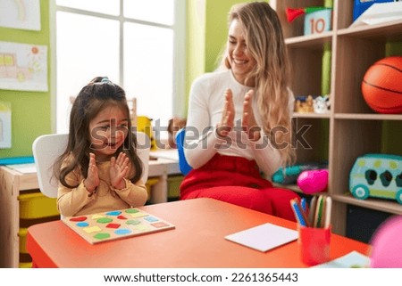 Teacher and toddler playing with maths puzzle game applauding at kindergarten