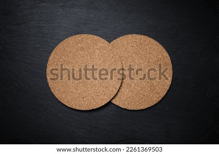Photo of two blank cork beer coasters on black stone slate plate. Copy space for text. Flat lay.