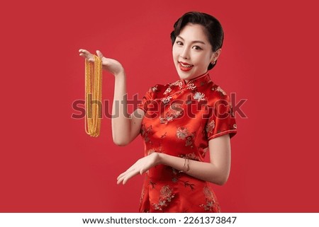 Chinese new year festival, Beautiful Young asian woman wearing traditional cheongsam qipao dress with gold necklaces on red background, Royalty-Free Stock Photo #2261373847