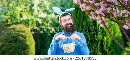 Horizontal photo banner for website header design. Funny man hunting easter eggs. Happy Easter concept. Man with beard, white ears of rabbit and basket with easter eggs on spring background.