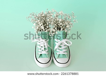 Beautiful casual shoes with flowers inside light background. Flowers in sneakers. Walk. Modern unisex footwear, sneakers. Fashionable stylish sports casual shoes. High quality photo